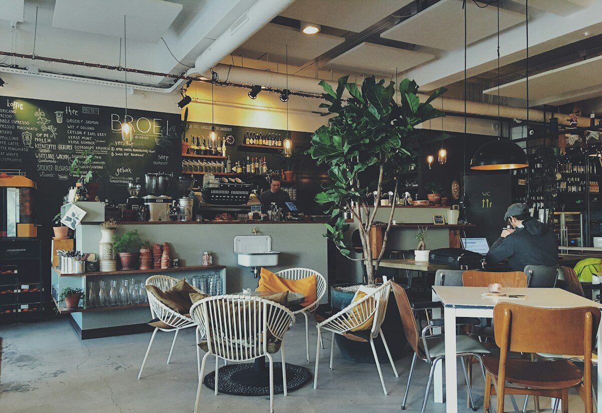 A warm café interior with plants, wooden chairs, and a chalkboard menu