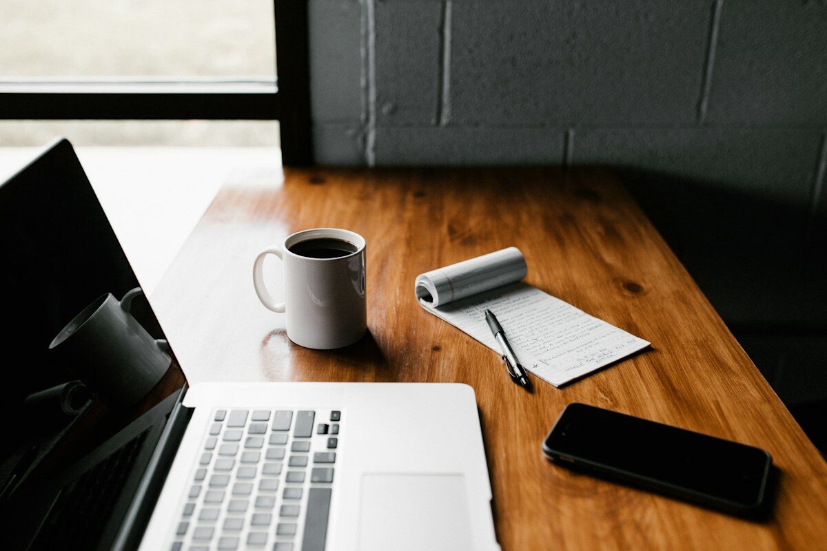 A laptop, notebook, and coffee on a wooden desk